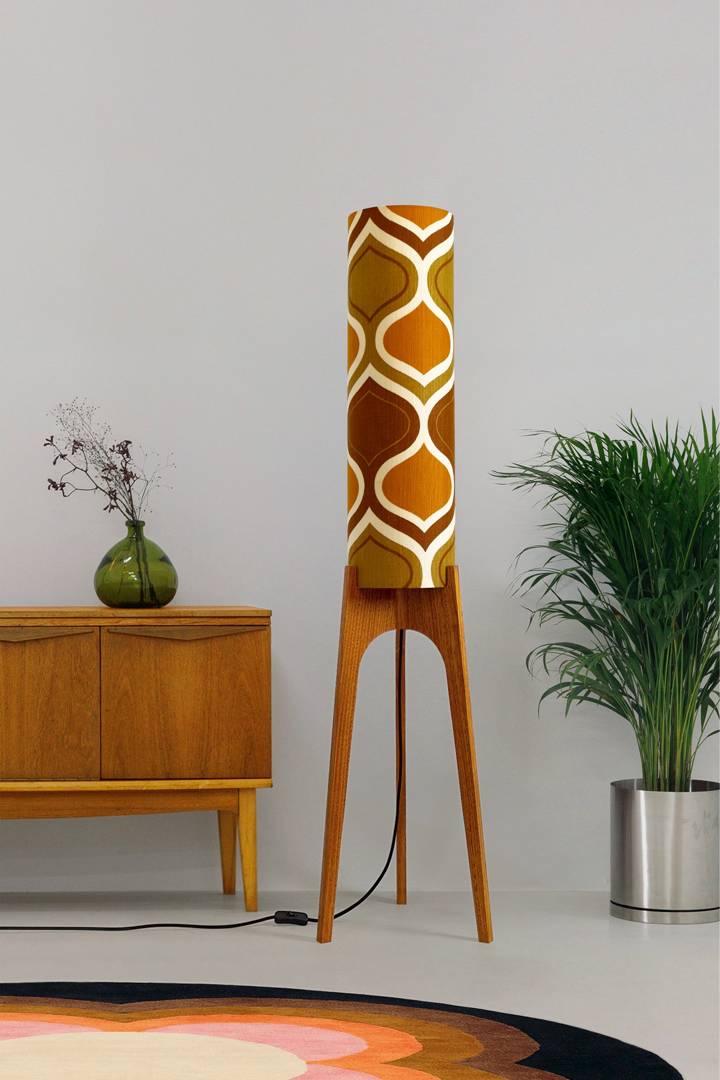The Honey Mustard Archie Rocket Floor Lamp is a playful nod to the geometric patterns of the 1970s. Handcrafted from authentic vintage fabric and hardwood oak next to a wooden cabinet and plant.