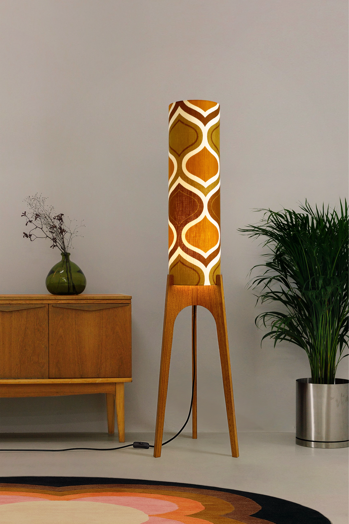 The Honey Mustard Archie Rocket Floor Lamp is a playful nod to the geometric patterns of the 1970s. Handcrafted from authentic vintage fabric and hardwood oak next to a wooden cabinet and plant.