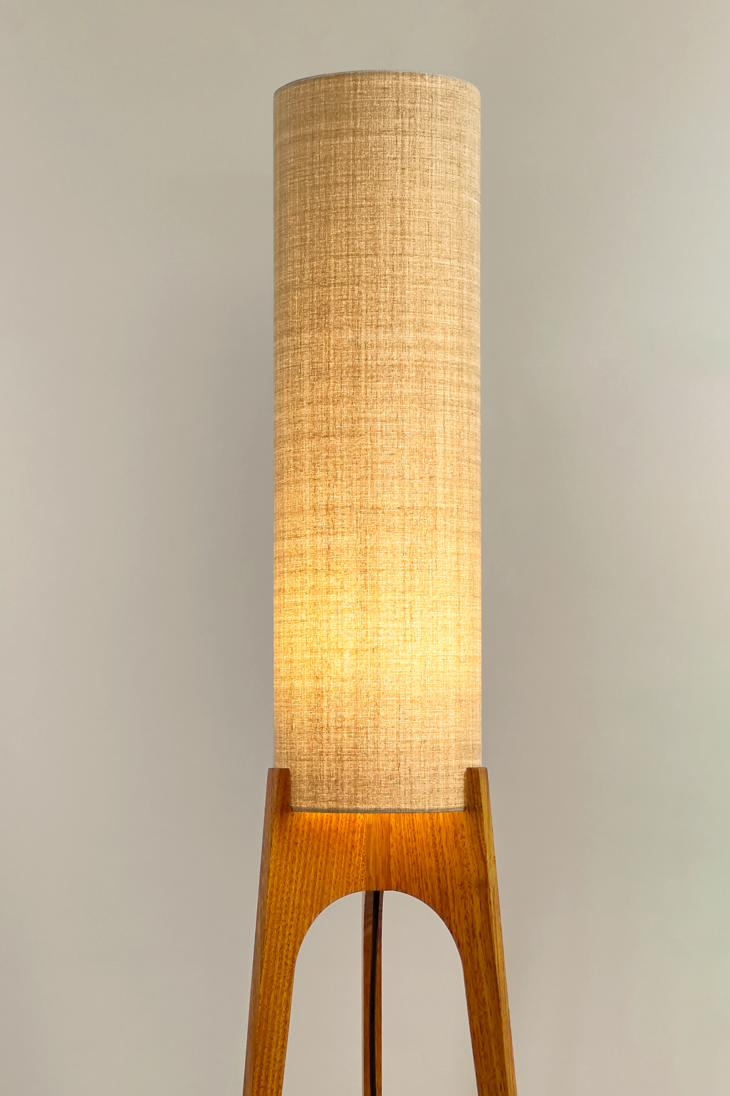 The Linen Archie Rocket Floor Lamp by Retro Duo, featuring a handcrafted wooden base and beige cylindrical shade, styled beside a wooden cabinet and plant against a light grey background.