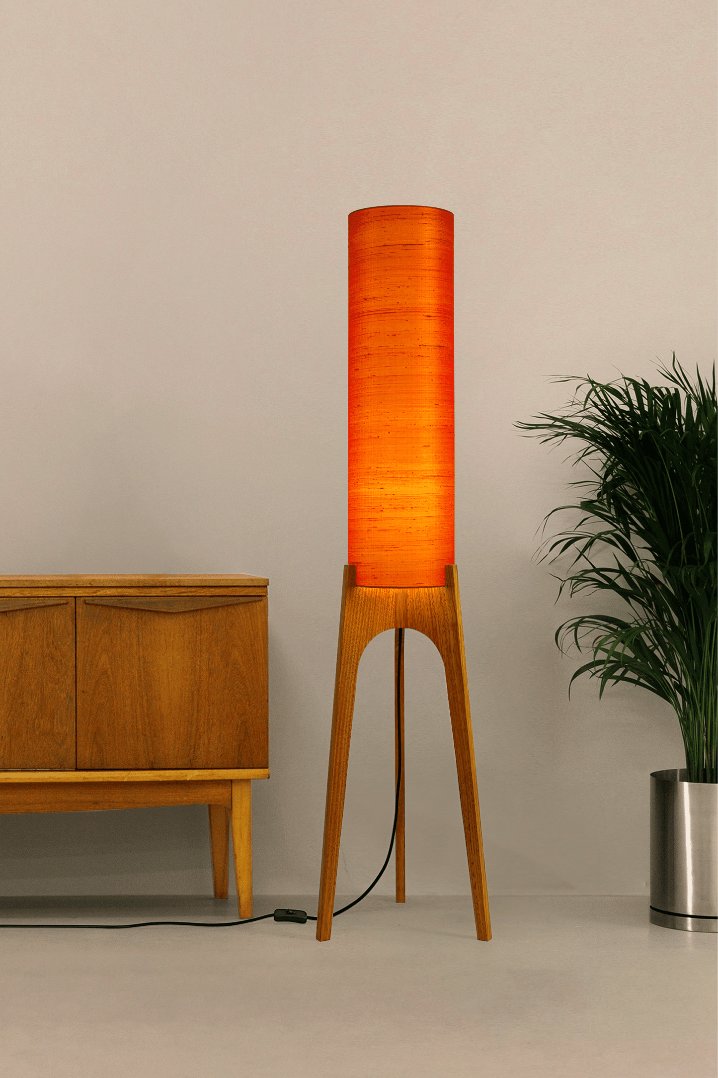 Wooden Rocket Floor Lamp with Orange cylindrical handmade lampshade with premium raw silk, next to a wooden cabinet and plant on a light grey background