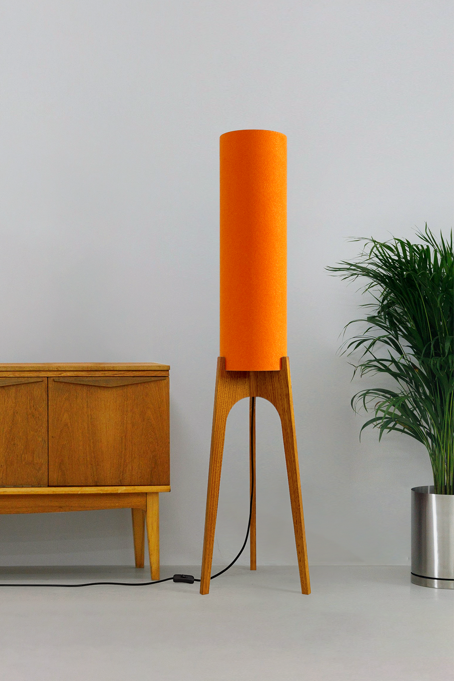 Orange - Archie Rocket Floor Lamp | Handmade by RETRO DUO with a cylindrical lampshade and wooden lamp base next to a cabinet & plant