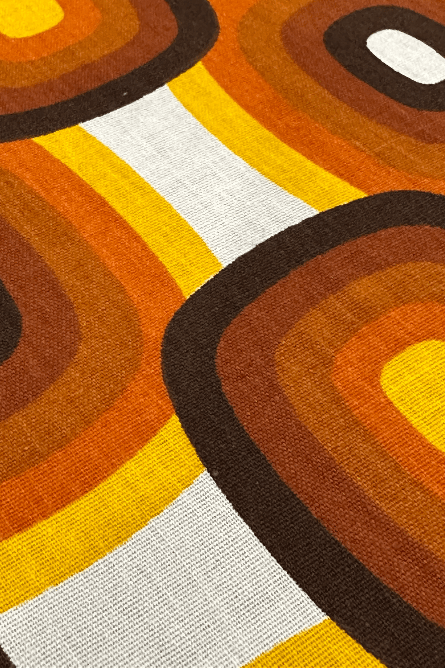 Close-up of a retro-style fabric with concentric circle pattern in brown, orange, and yellow on a white background.