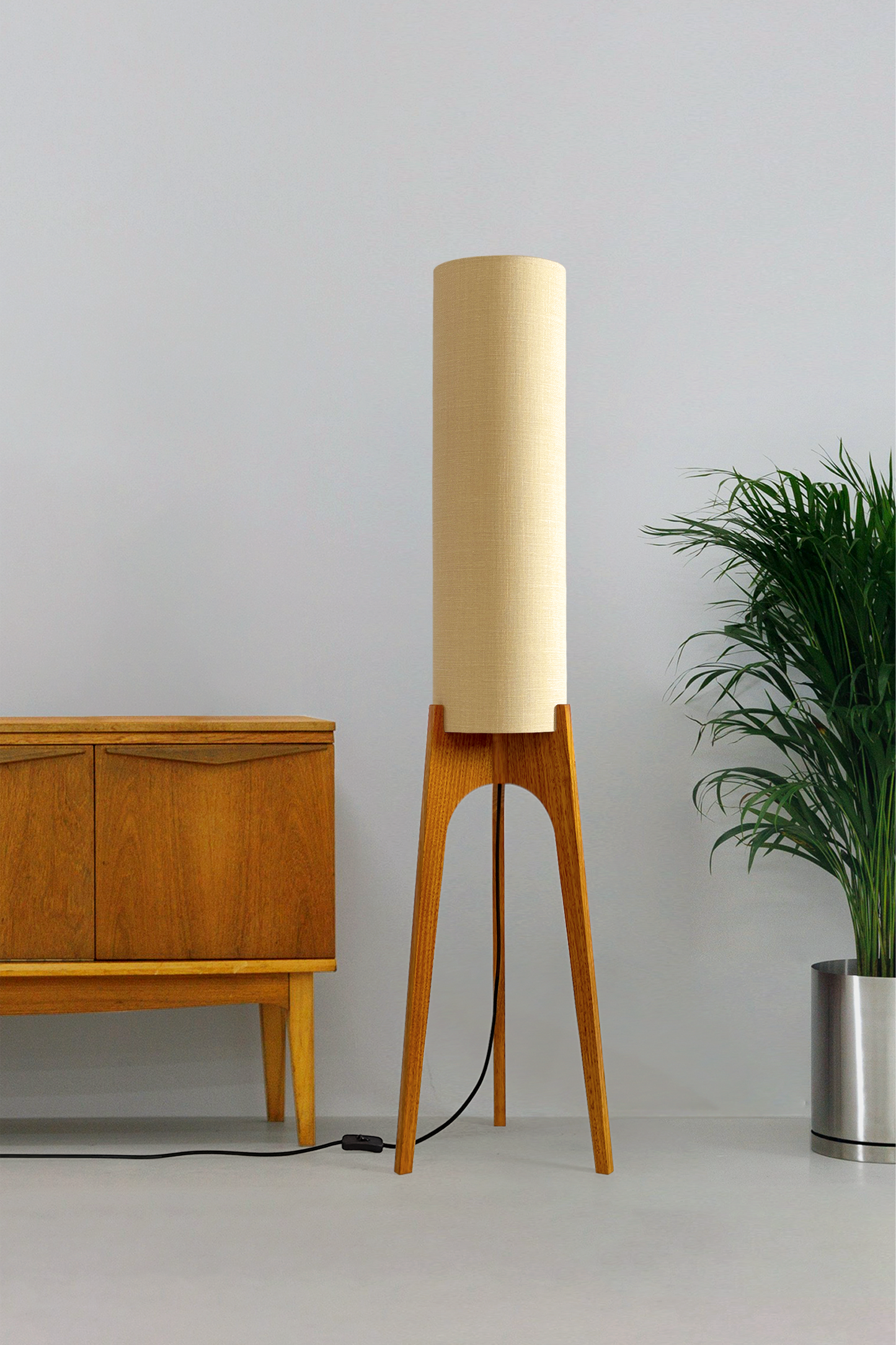 Sesame - Archie Rocket Floor Lamp by Retro Duo, featuring a handcrafted wooden base and beige cylindrical shade, styled beside a wooden cabinet and plant against a light grey background.