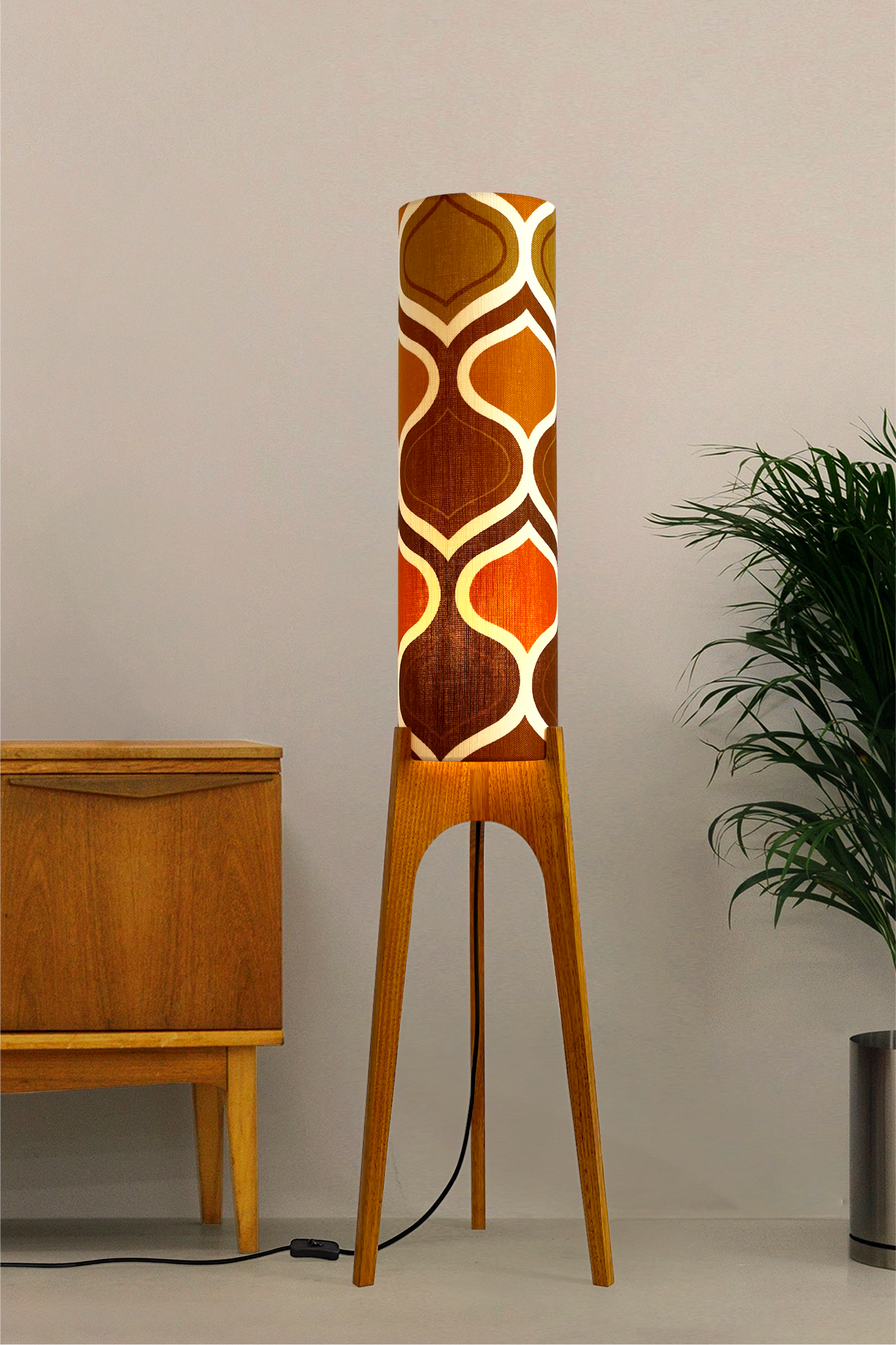The Tangerine Archie Rocket Floor Lamp is a playful nod to the geometric patterns of the 1970s. Handcrafted from authentic vintage fabric and hardwood oak with a patterned shade in a room setting with a cabinet and plant.
