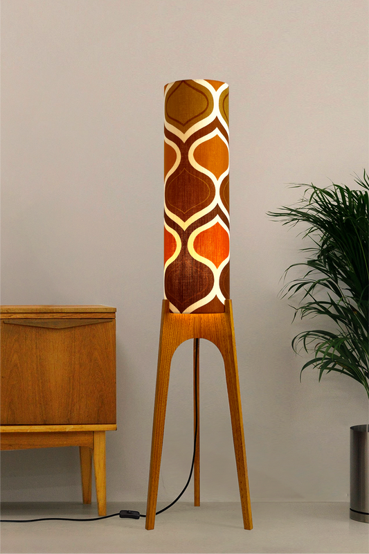 The Tangerine Archie Rocket Floor Lamp is a playful nod to the geometric patterns of the 1970s. Handcrafted from authentic vintage fabric and hardwood oak with a patterned shade in a room setting with a cabinet and plant.