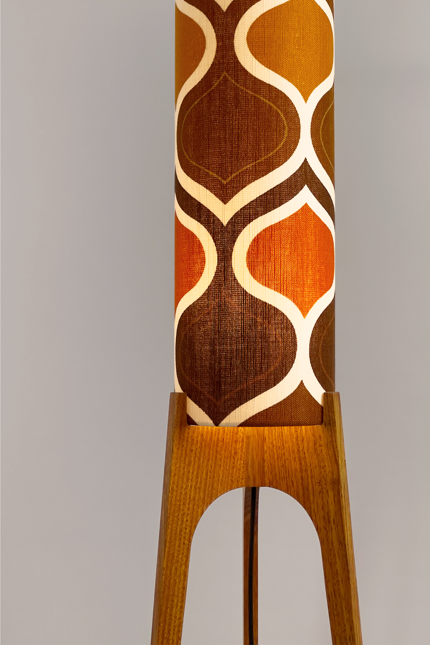 The Tangerine Archie Rocket Floor Lamp is a playful nod to the geometric patterns of the 1970s. Handcrafted from authentic vintage fabric and hardwood oak with a patterned shade in a room setting with a cabinet and plant.