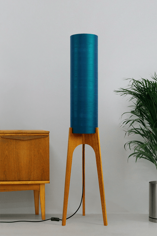 Wooden Rocket Floor Lamp with Teal Blue cylindrical handmade lampshade with premium raw silk, next to a wooden cabinet and plant on a light grey background