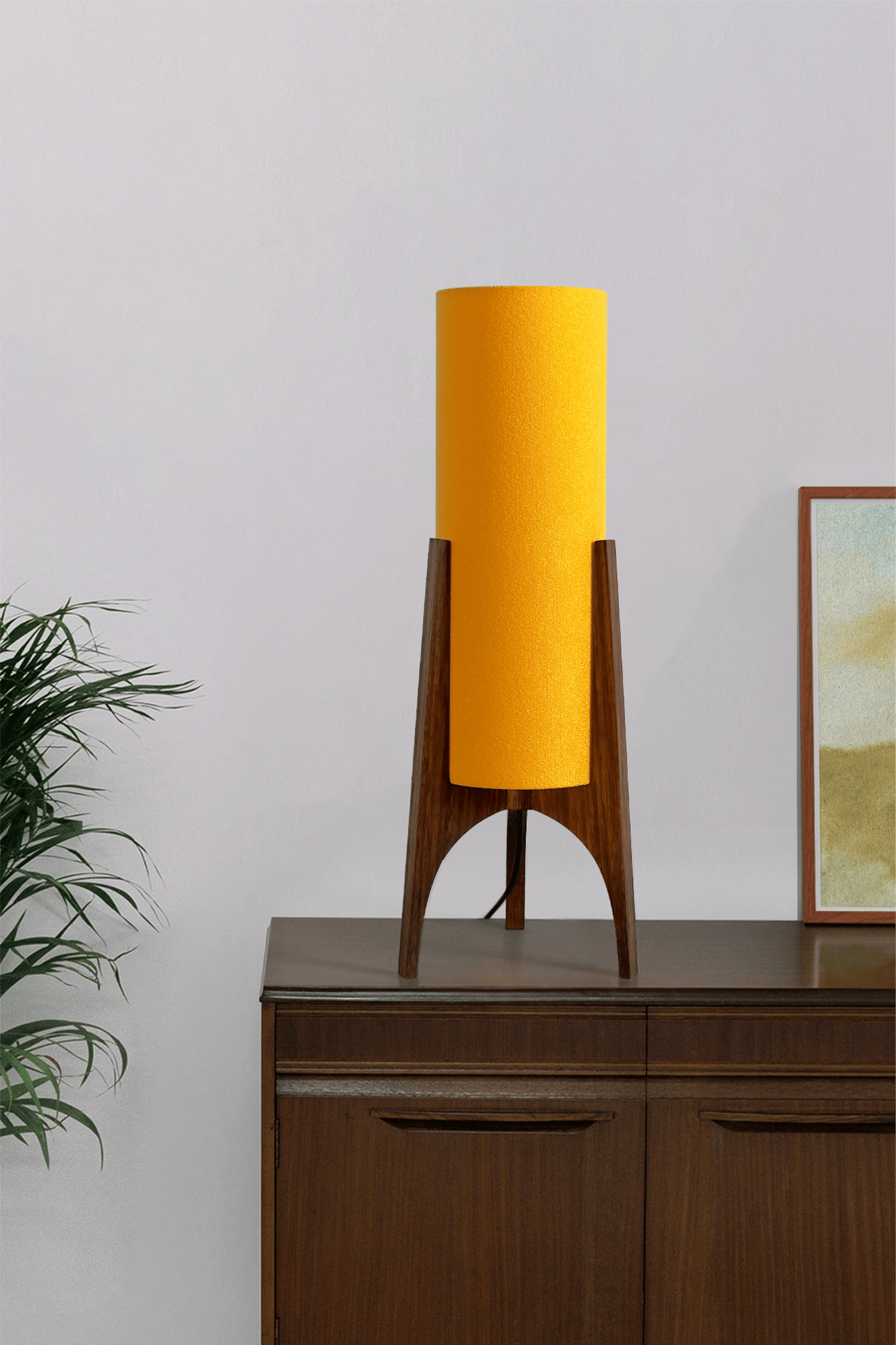 Canary Archie Rocket table lamp on a wooden cabinet with a plant and framed picture in the background.