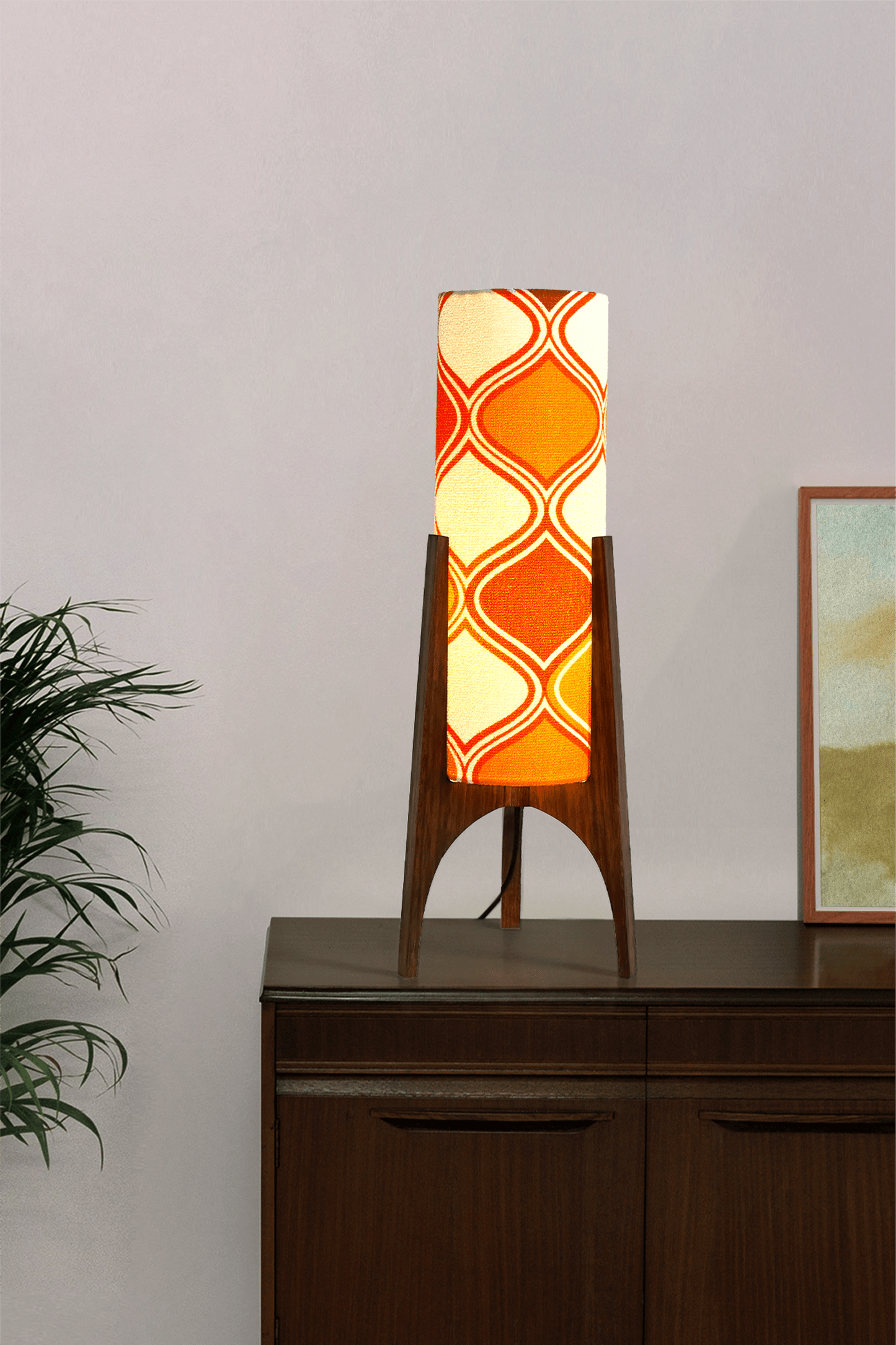 Archie Rocket Table lamp with a vintage geometric pattern fabric in orange and white shade on a wooden cabinet against a plain wall.