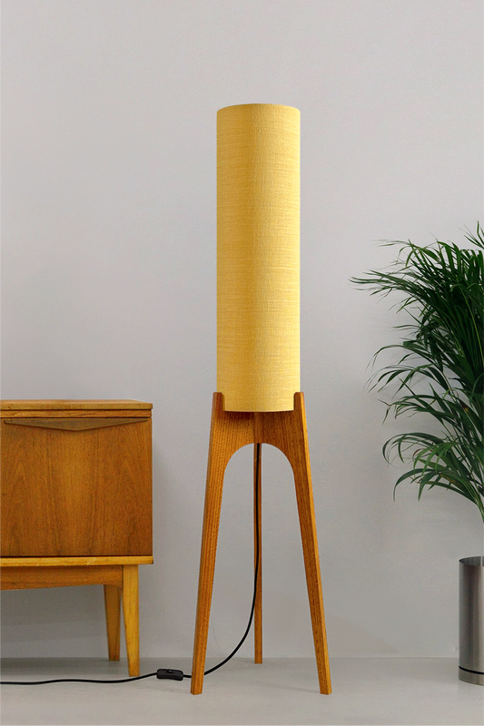 Wooden Rocket floor lamp with a premium linen shade in Wheat next to a wooden cabinet and plant on a beige background
