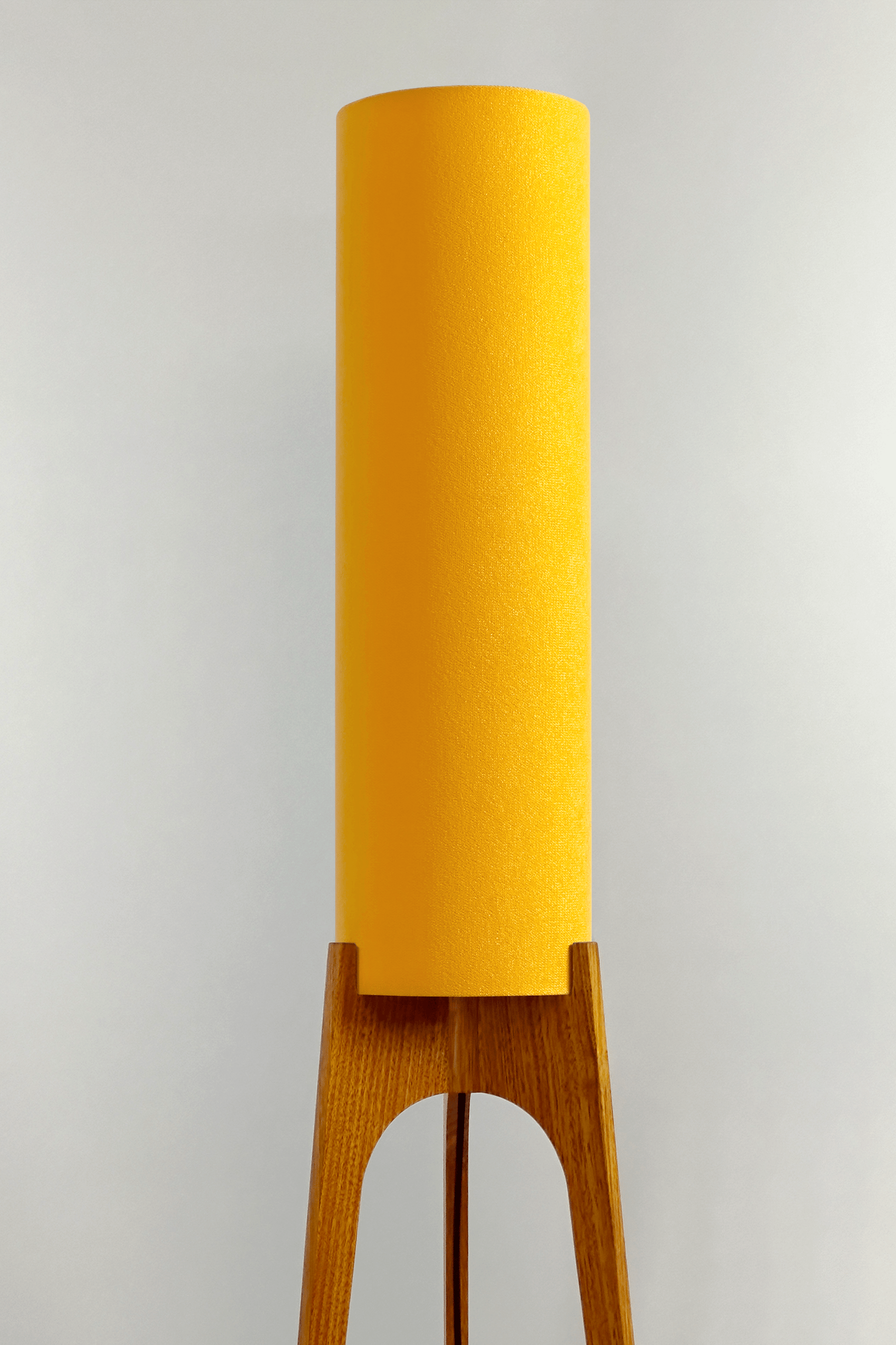 Yellow rocket floor lamp with wooden base against a wall 