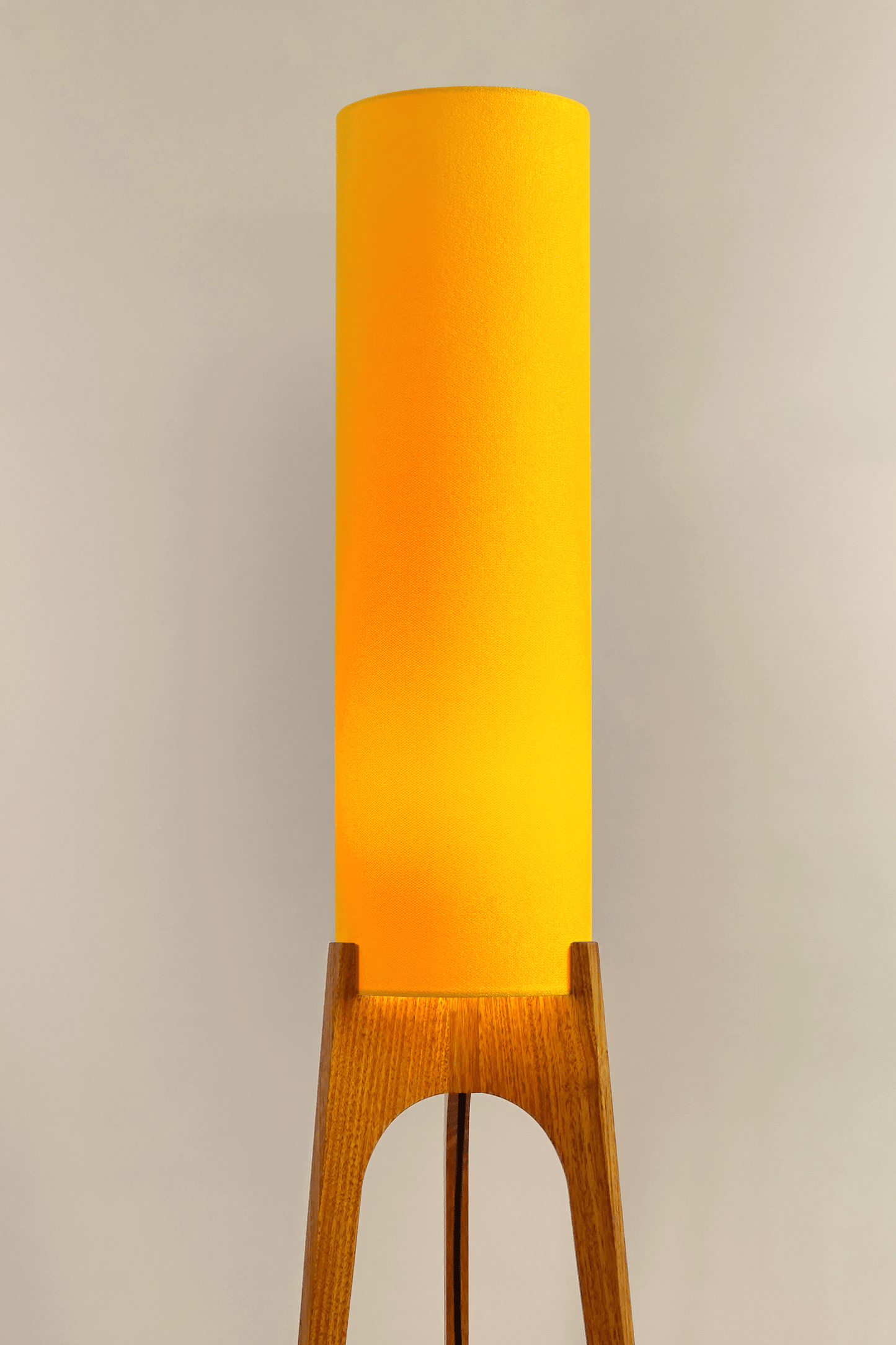 Yellow rocket floor lamp with wooden base against a wall 