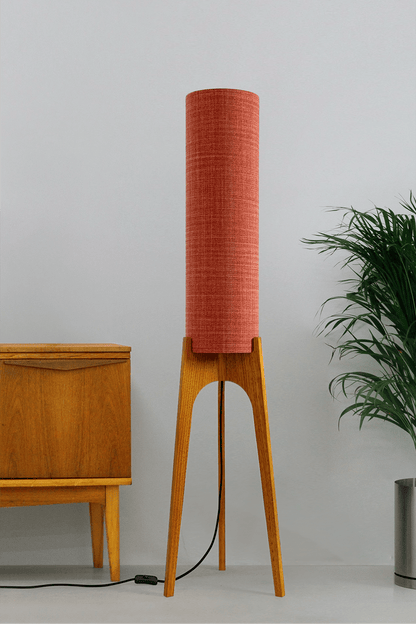 Chili - Tall Archie Rocket floor lamp with red cylindrical shade and wooden base next to a wooden cabinet and plant.