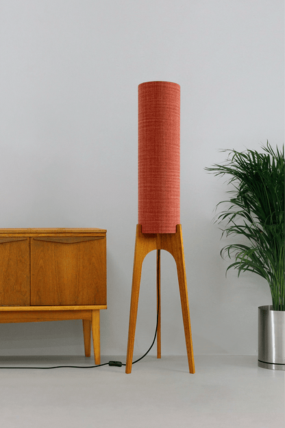 Chili - Tall Archie Rocket floor lamp with red cylindrical shade and wooden base next to a wooden cabinet and plant.