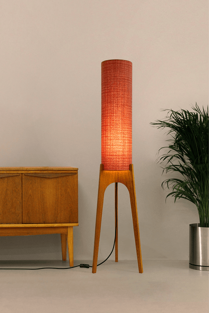 Chili - Tall Archie Rocket floor lamp with red cylindrical shade and wooden base next to a wooden cabinet and plant.