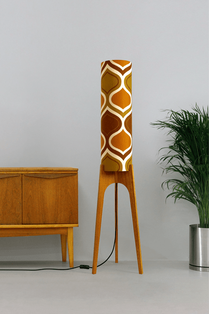 Honey Mustard - Archie Rocket Wooden Floor Lamp with a handmade lampshade with  vintage fabric in geometric patterns next to a wooden cabinet and plant on a light grey background