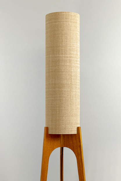 The Linen Archie Rocket Floor Lamp by Retro Duo, featuring a handcrafted wooden base and beige cylindrical shade, styled beside a wooden cabinet and plant against a light grey background.