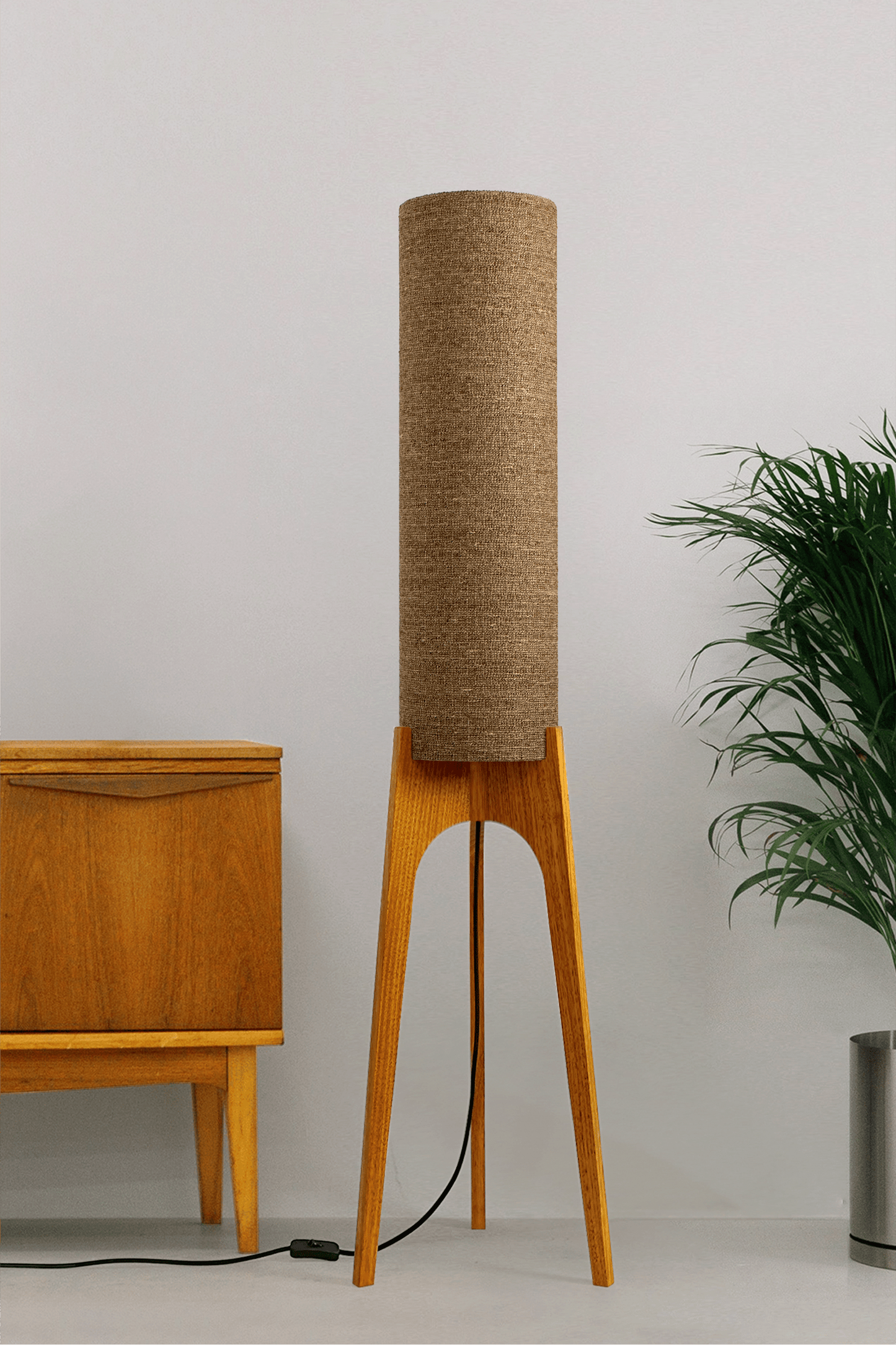 a handmade Rocket Floor Lamp with a woven lampshade in brown and a wooden lamp base in a mid-century room setting