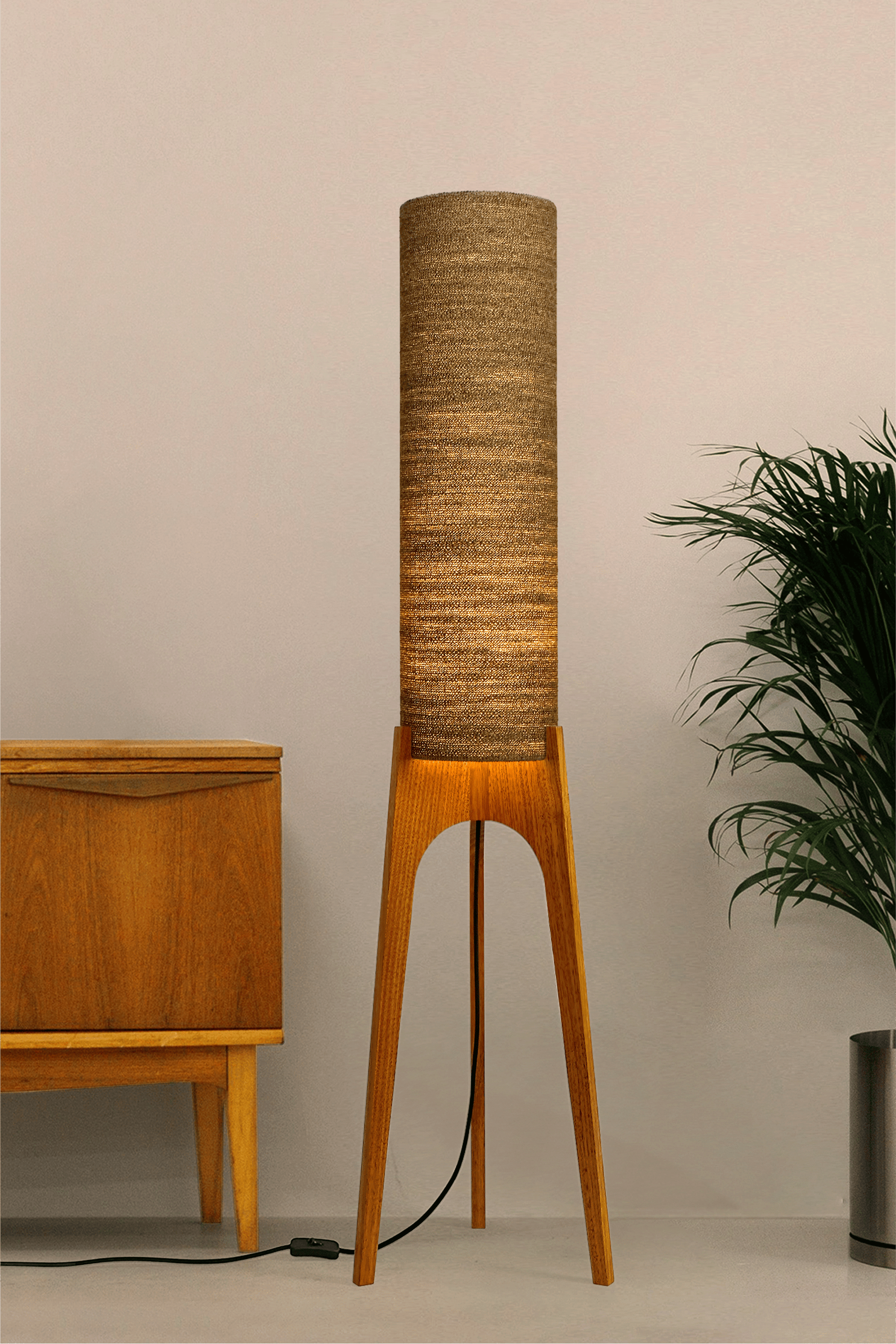 a handmade Rocket Floor Lamp with a woven lampshade in brown and a wooden lamp base in a mid-century room setting