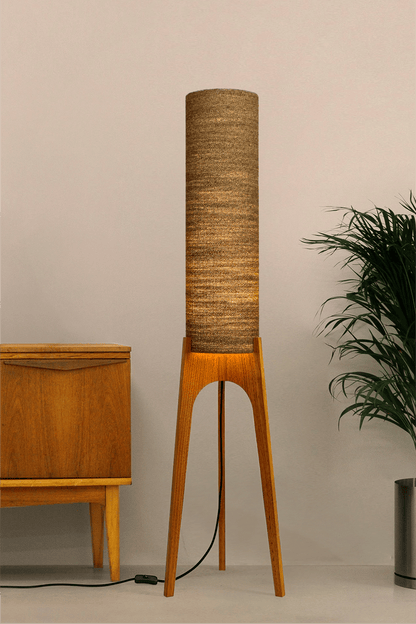 a handmade Rocket Floor Lamp with a woven lampshade in brown and a wooden lamp base in a mid-century room setting