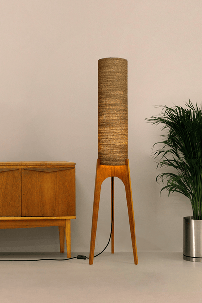 a handmade Rocket Floor Lamp with a woven lampshade in brown and a wooden lamp base in a mid-century room setting