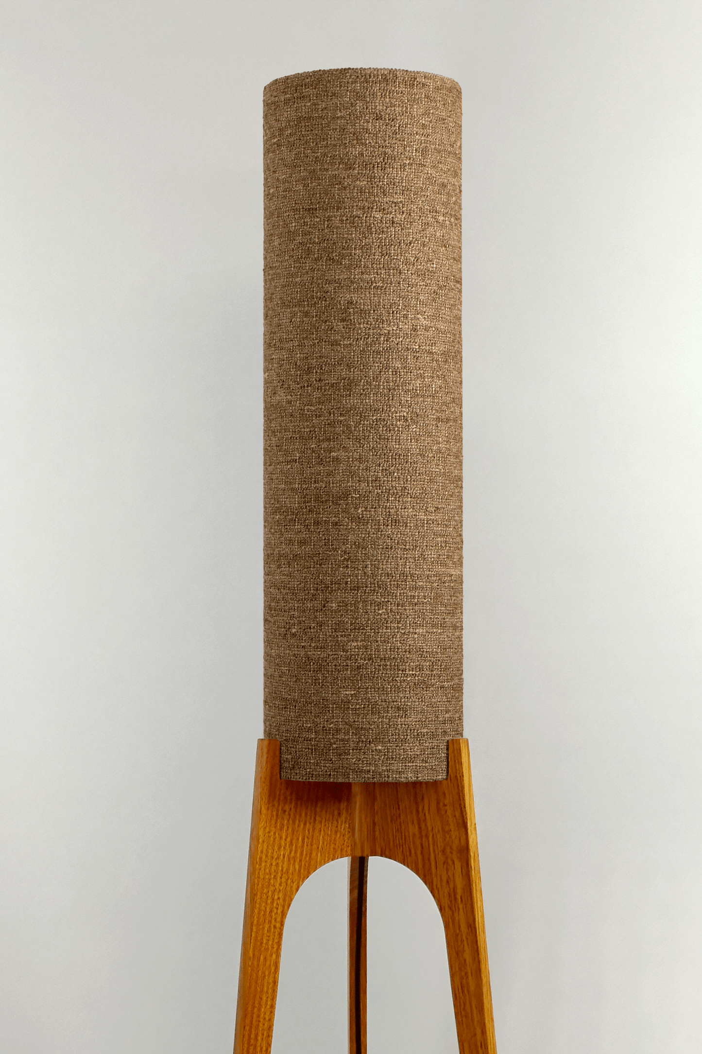 a handmade Rocket Floor Lamp with a woven lampshade in brown and a wooden lamp base in a mid-century room setting