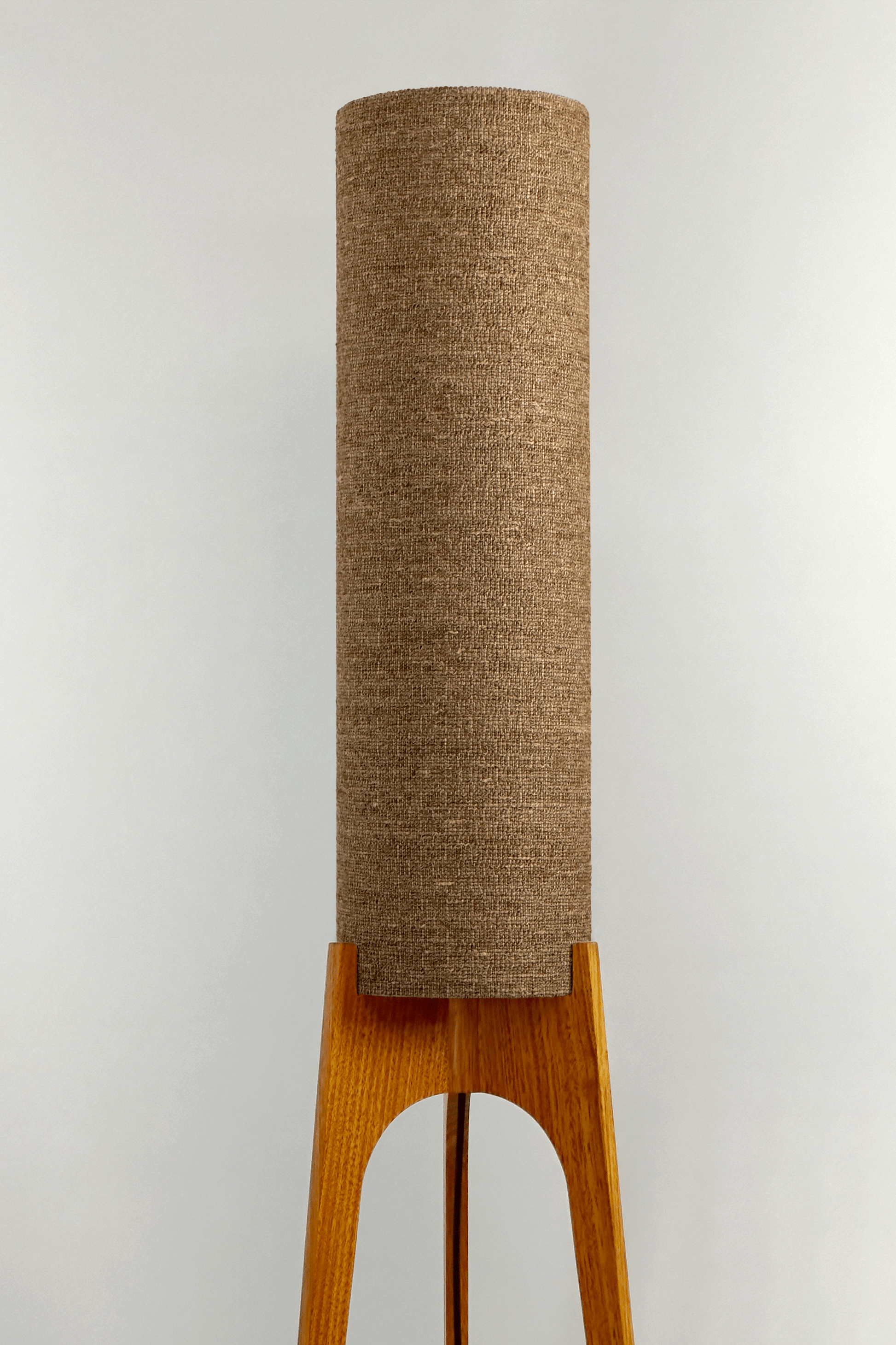a handmade Rocket Floor Lamp with a woven lampshade in brown and a wooden lamp base in a mid-century room setting
