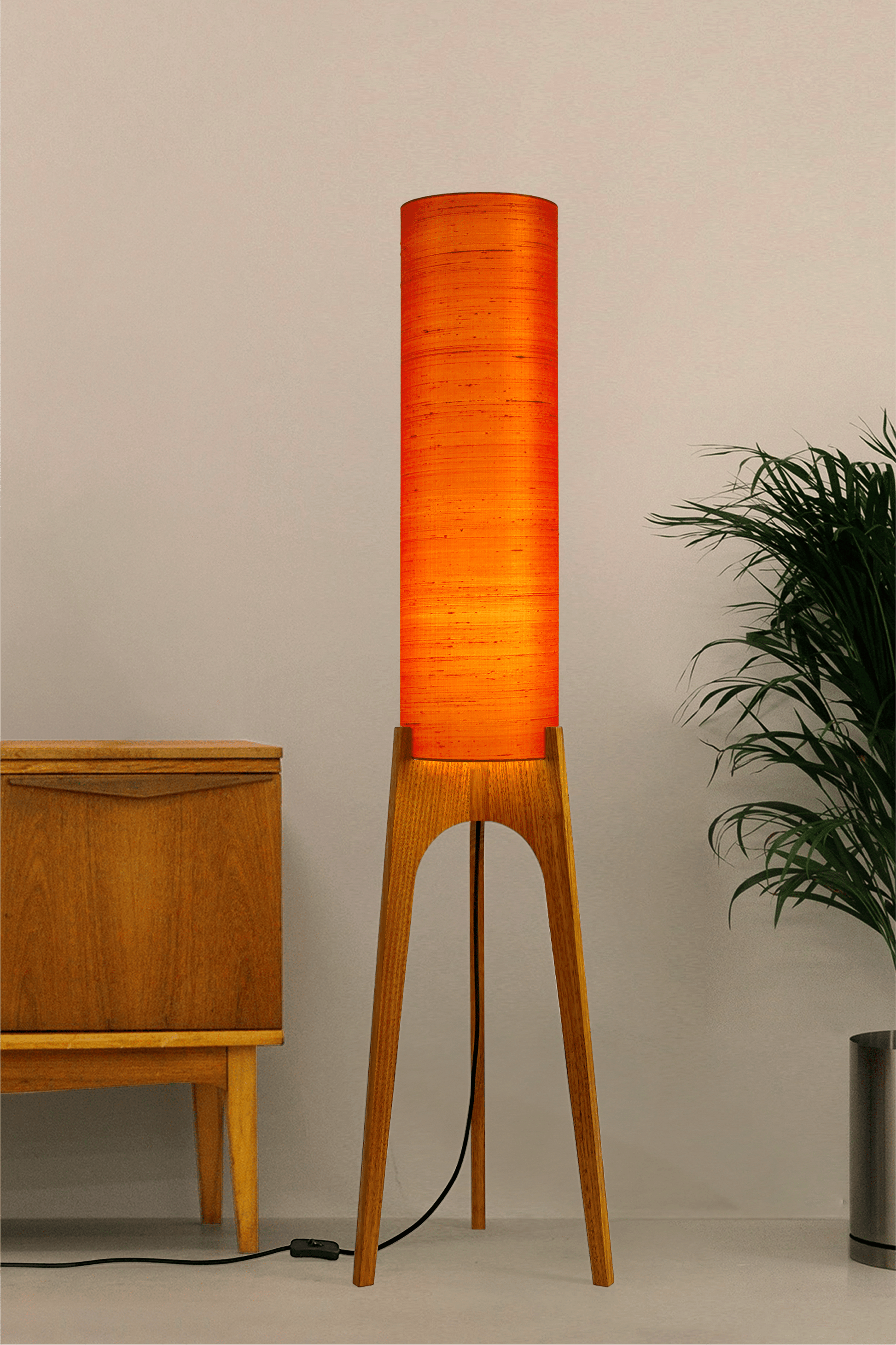 Wooden Rocket Floor Lamp with Orange cylindrical handmade lampshade with premium raw silk, next to a wooden cabinet and plant on a light grey background