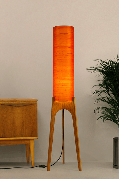 Wooden Rocket Floor Lamp with Orange cylindrical handmade lampshade with premium raw silk, next to a wooden cabinet and plant on a light grey background