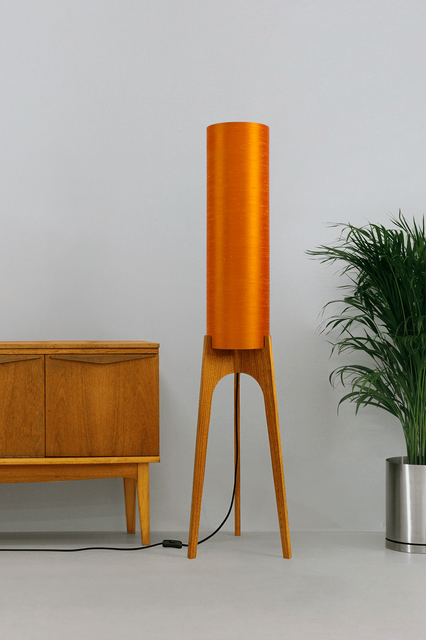 Wooden Rocket Floor Lamp with Orange cylindrical handmade lampshade with premium raw silk, next to a wooden cabinet and plant on a light grey background