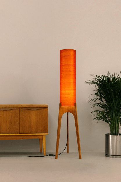 Wooden Rocket Floor Lamp with Orange cylindrical handmade lampshade with premium raw silk, next to a wooden cabinet and plant on a light grey background