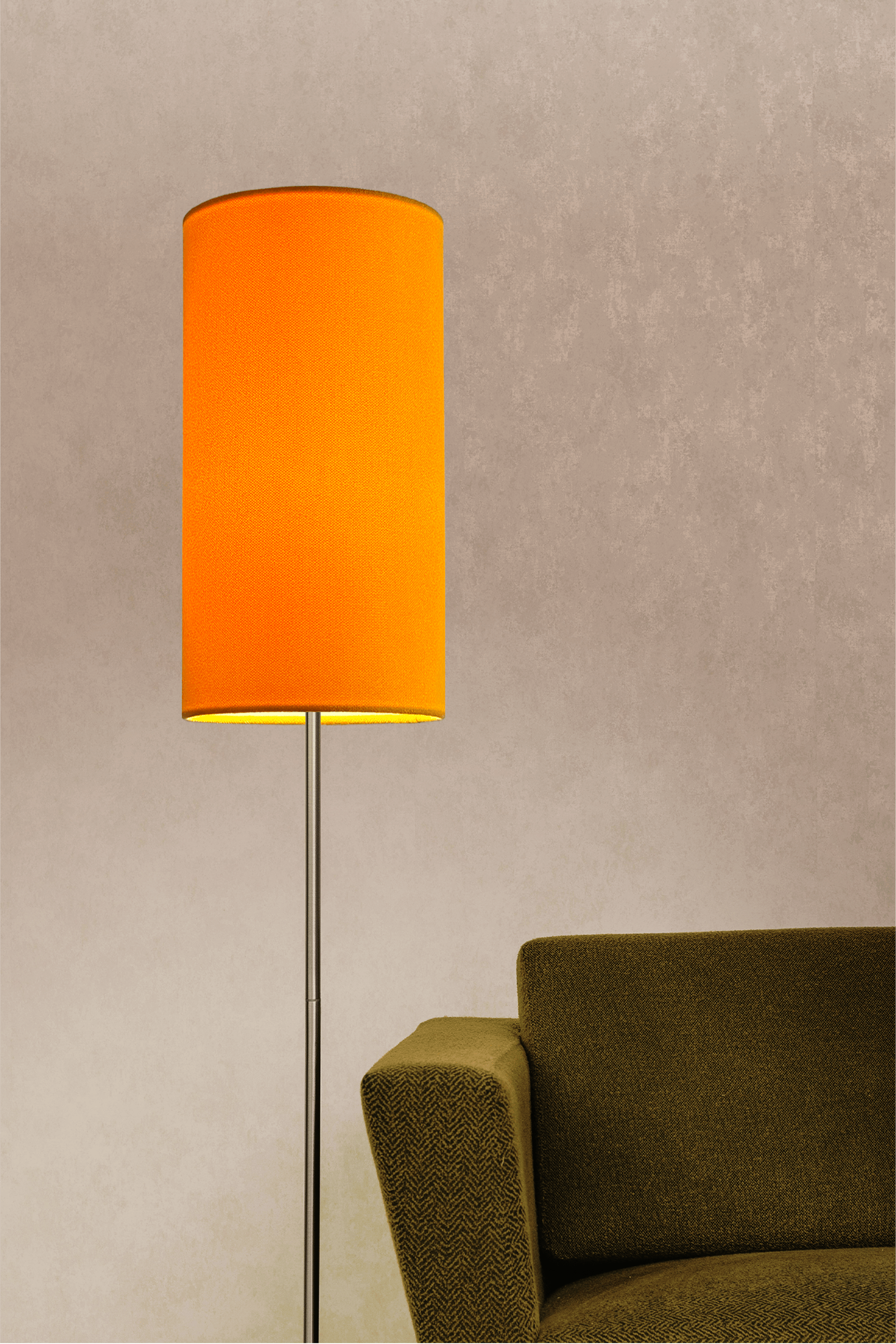 Yellow lampshade on a floor lamp next to a green sofa against a beige wall