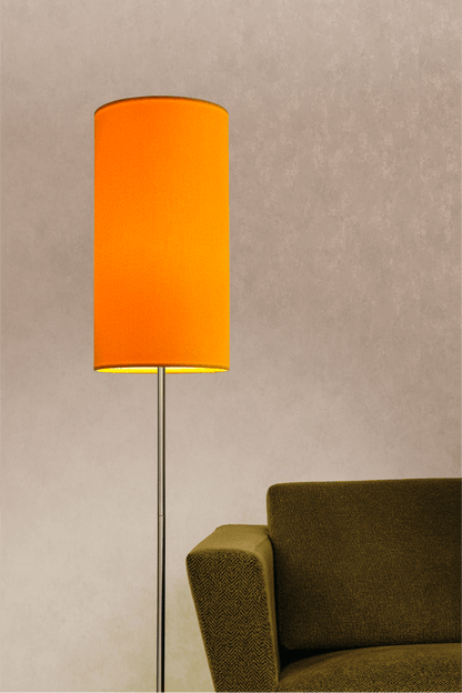 Yellow lampshade on a floor lamp next to a green sofa against a beige wall