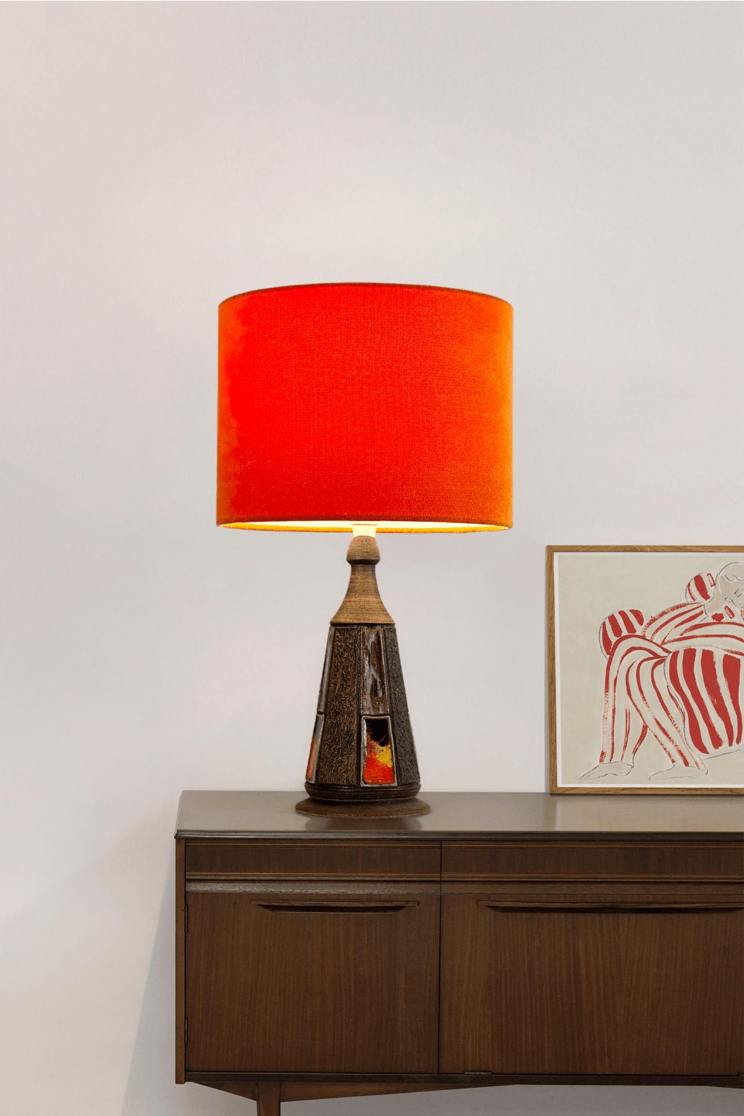 Table lamp with a Orange shade on a wooden sideboard against a white wall.