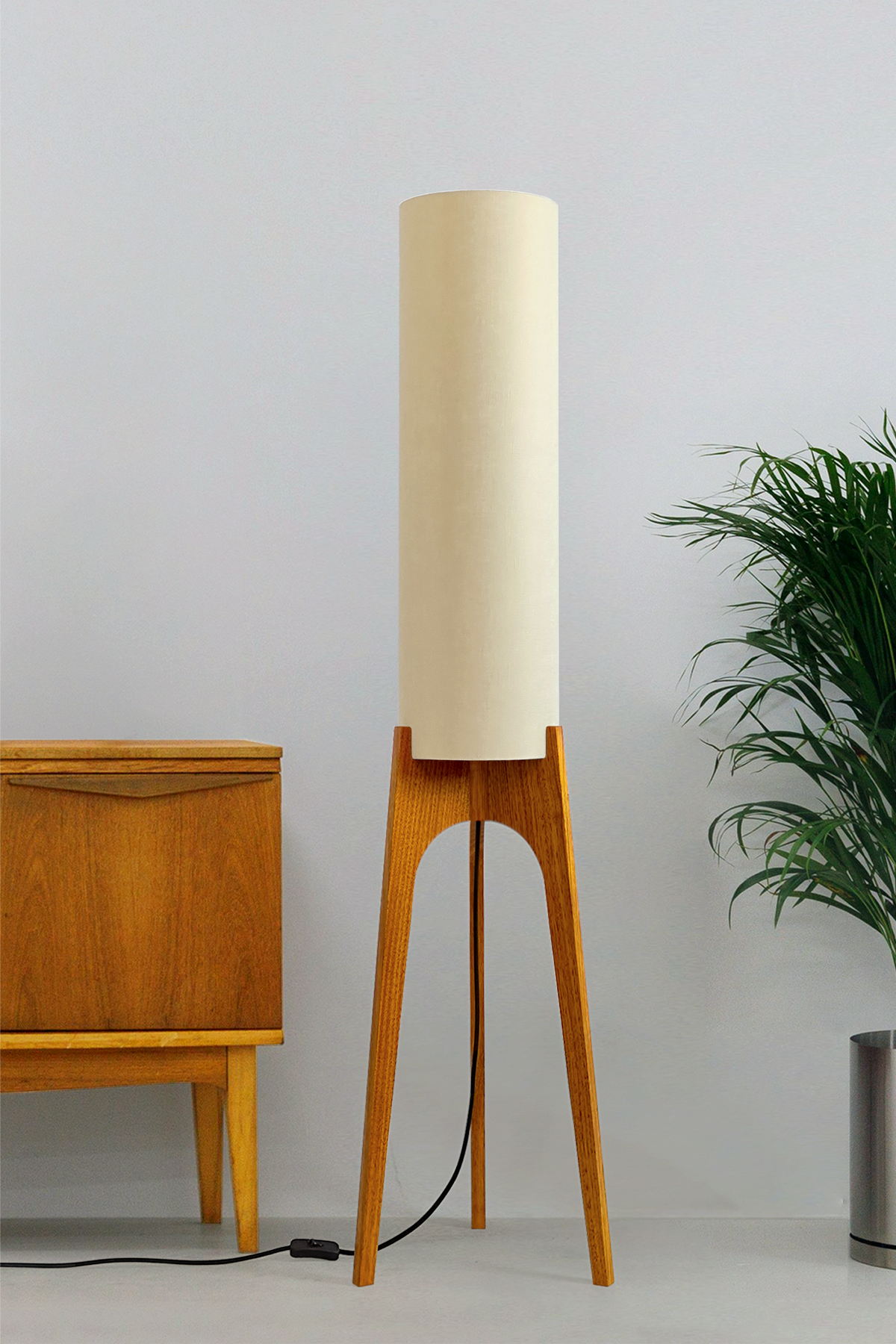 Sesame - Archie Rocket Floor Lamp by Retro Duo, featuring a handcrafted wooden base and beige cylindrical shade, styled beside a wooden cabinet and plant against a light grey background.