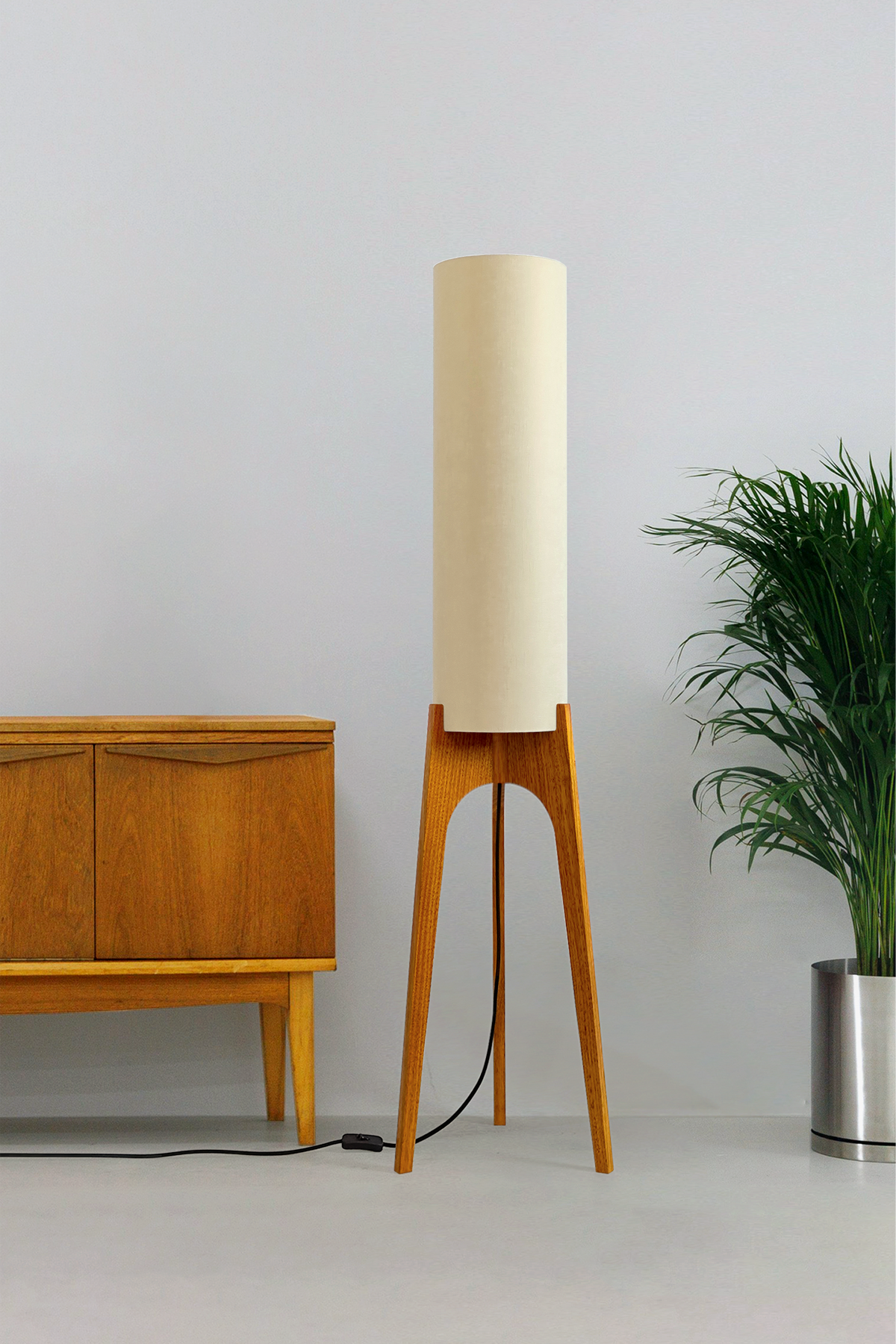 Sesame - Archie Rocket Floor Lamp by Retro Duo, featuring a handcrafted wooden base and beige cylindrical shade, styled beside a wooden cabinet and plant against a light grey background.