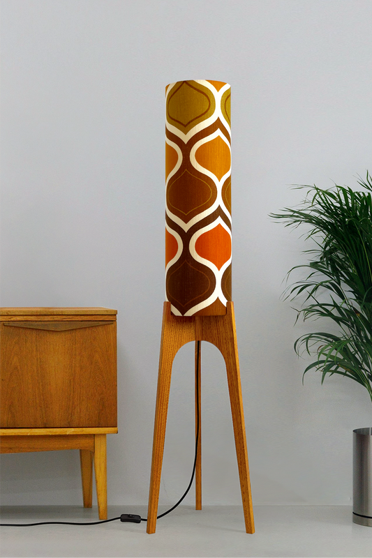 The Tangerine Archie Rocket Floor Lamp is a playful nod to the geometric patterns of the 1970s. Handcrafted from authentic vintage fabric and hardwood oak with a patterned shade in a room setting with a cabinet and plant.