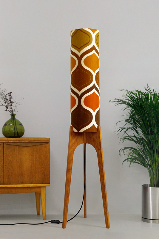 The Tangerine Archie Rocket Floor Lamp is a playful nod to the geometric patterns of the 1970s. Handcrafted from authentic vintage fabric and hardwood oak with a patterned shade in a room setting with a cabinet and plant.