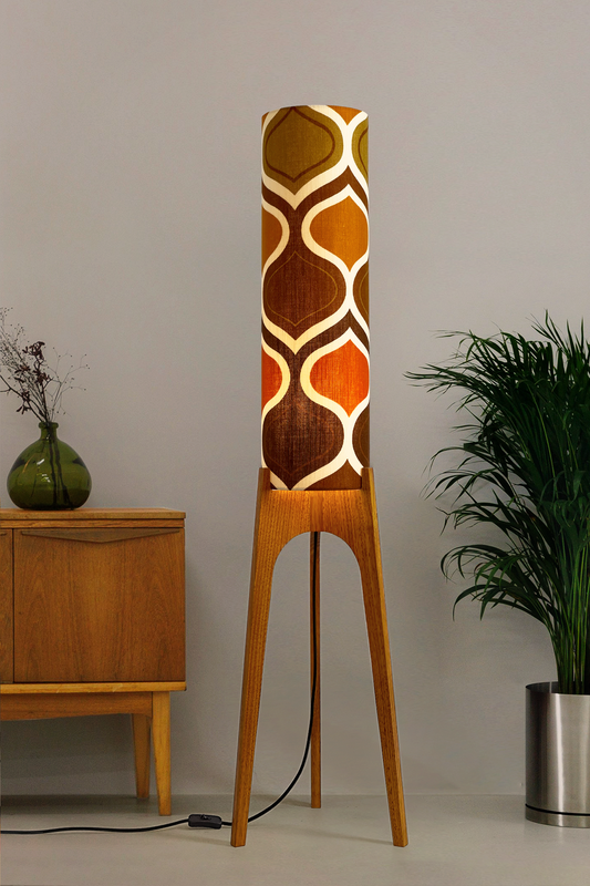 The Tangerine Archie Rocket Floor Lamp is a playful nod to the geometric patterns of the 1970s. Handcrafted from authentic vintage fabric and hardwood oak with a patterned shade in a room setting with a cabinet and plant.