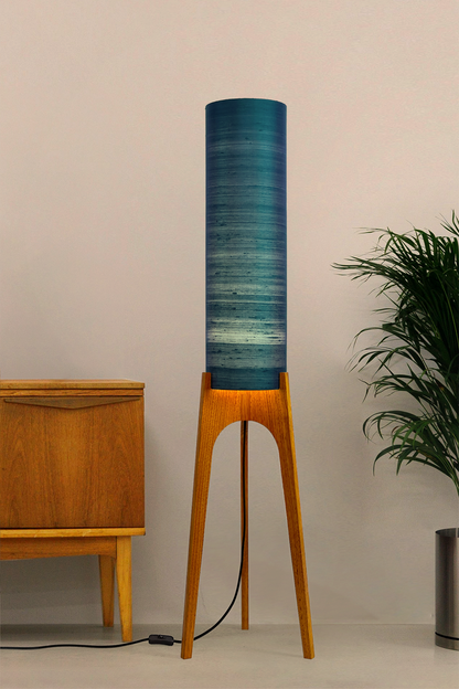 Wooden Rocket Floor Lamp with Teal Blue cylindrical handmade lampshade with premium raw silk, next to a wooden cabinet and plant on a light grey background