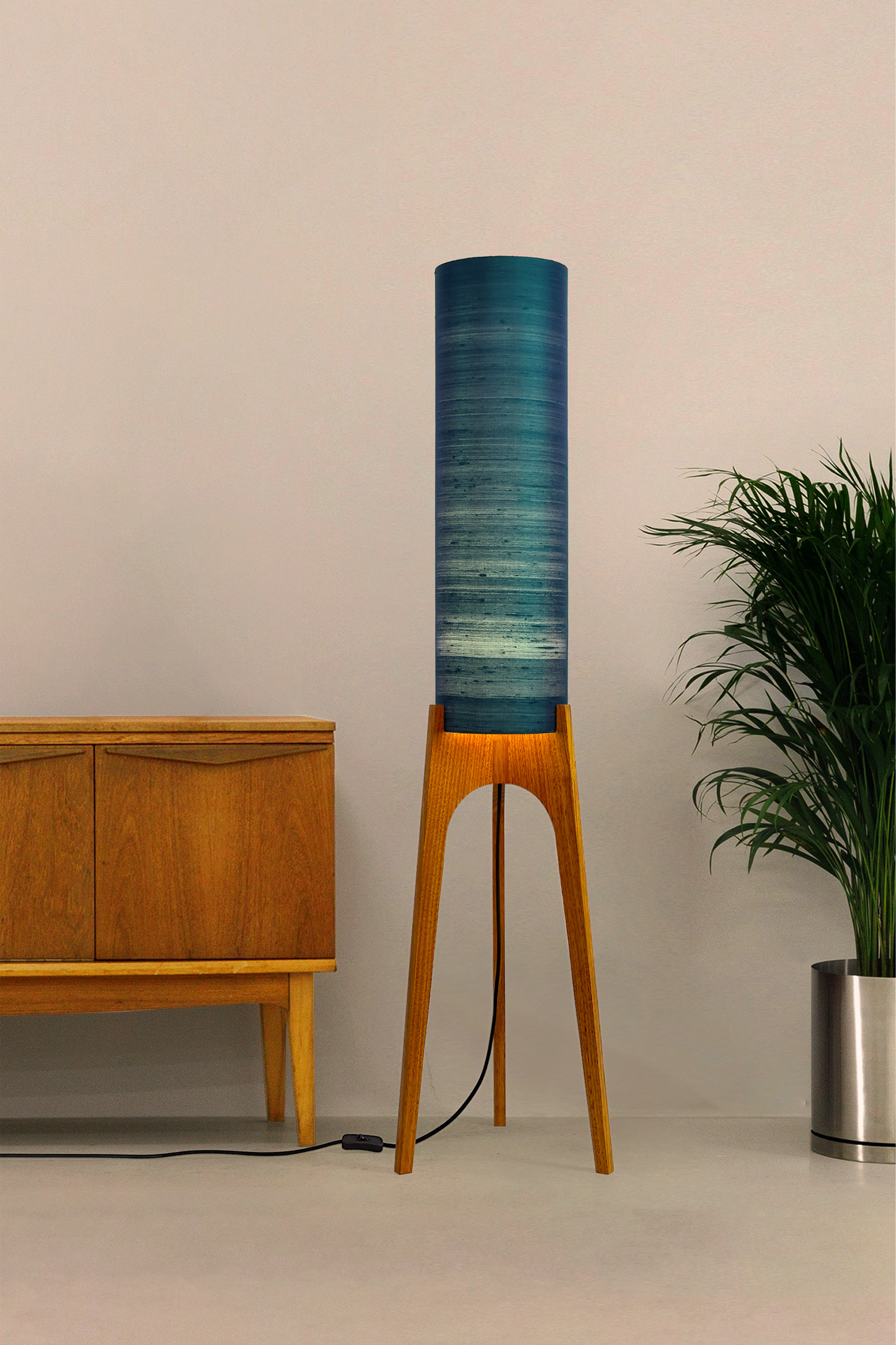 Wooden Rocket Floor Lamp with Teal Blue cylindrical handmade lampshade with premium raw silk, next to a wooden cabinet and plant on a light grey background