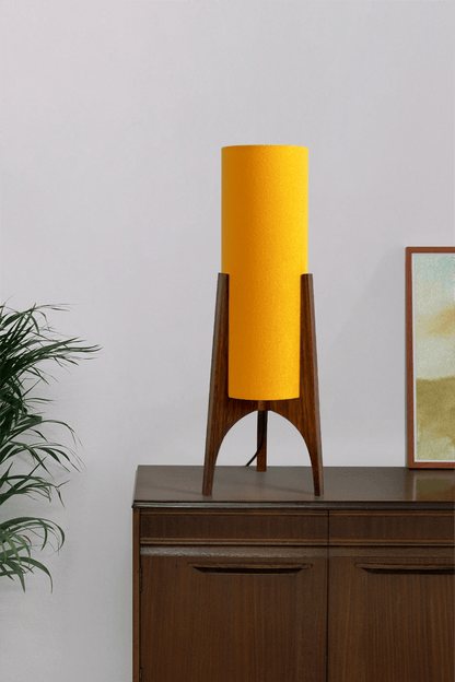 Canary Archie Rocket table lamp on a wooden cabinet with a plant and framed picture in the background.
